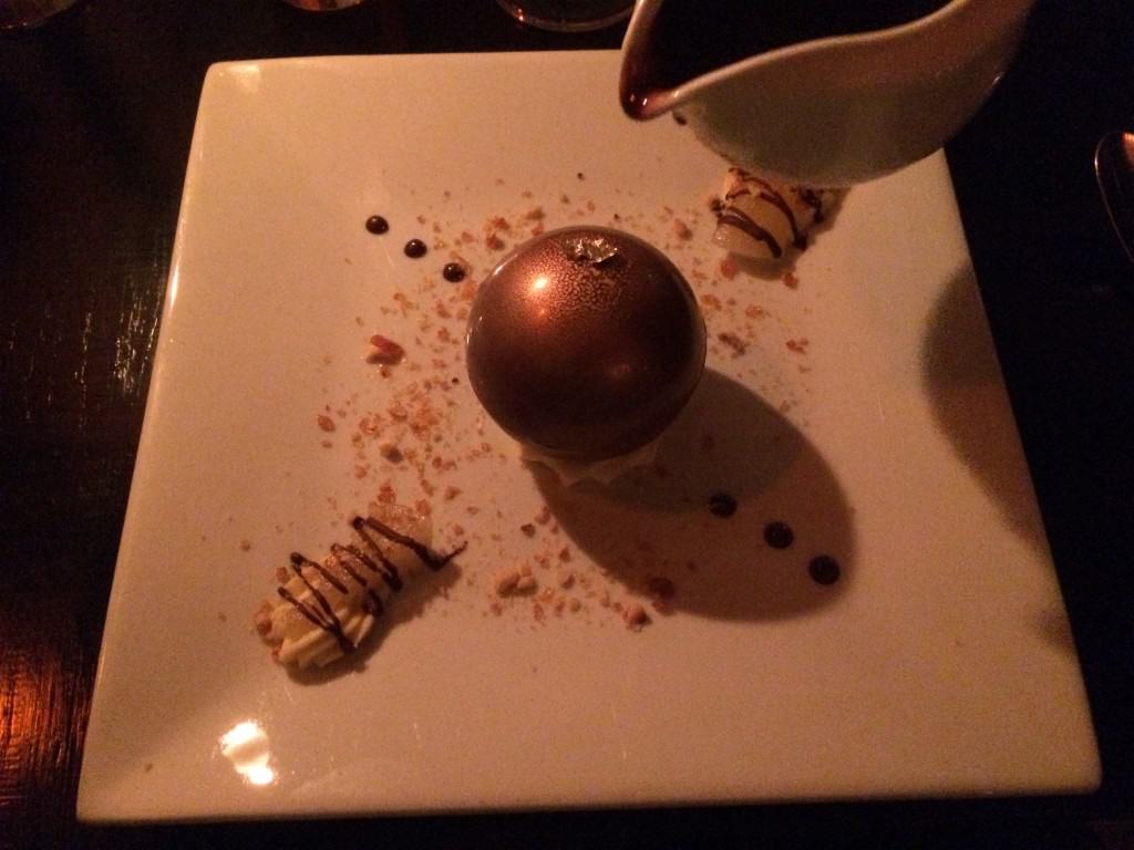 orb af mørk chokolade med guld på toppen, pære, mynte og vaniljeis indeni, karameliserede hasselnødder og varm chokoladesauce