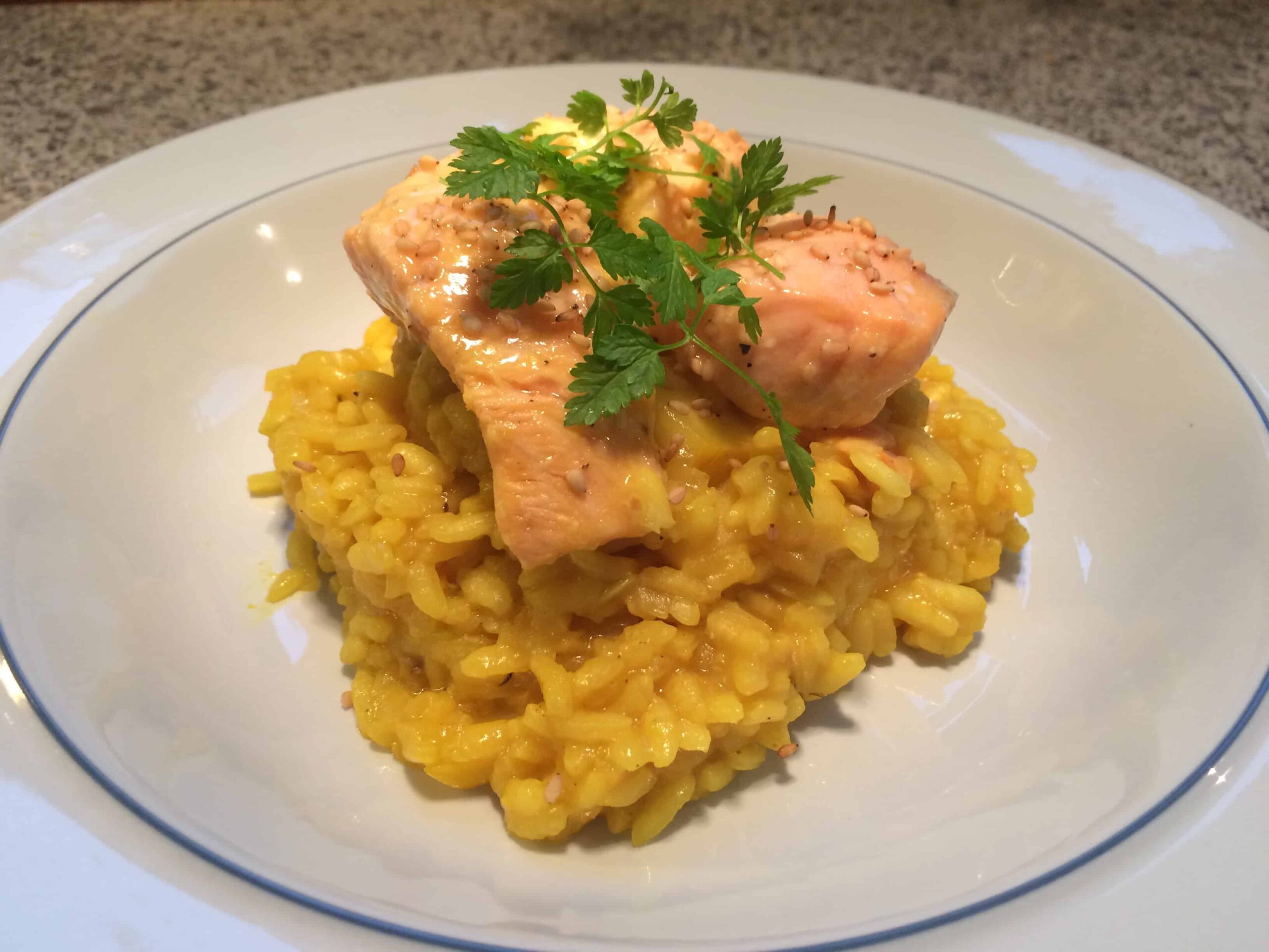 Gul ingefærrisotto med citronlaks pyntet med kørvel og sesamfrø på en hvid tallerken